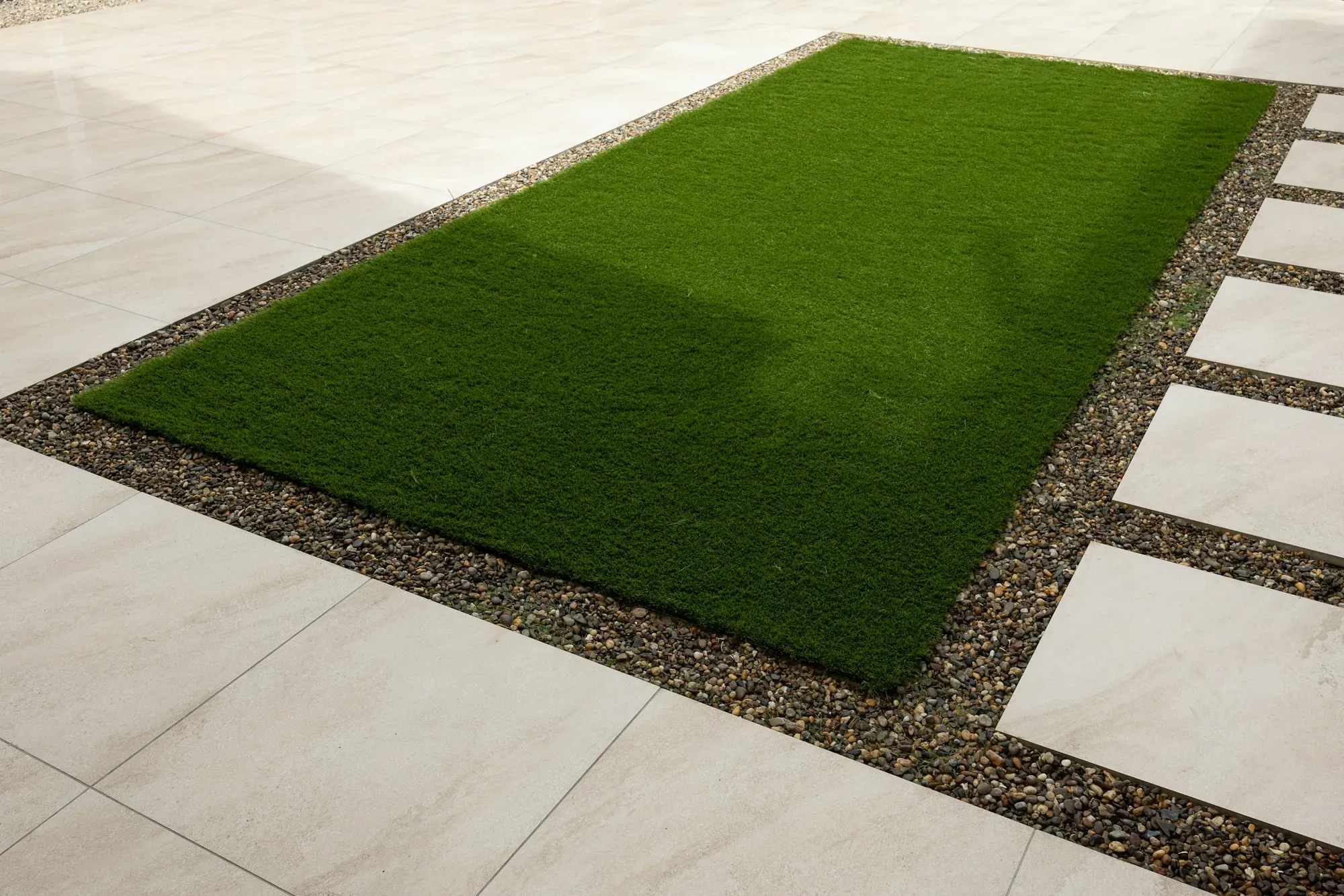 Artificial turf panel edged with gravel and pale stone pavers