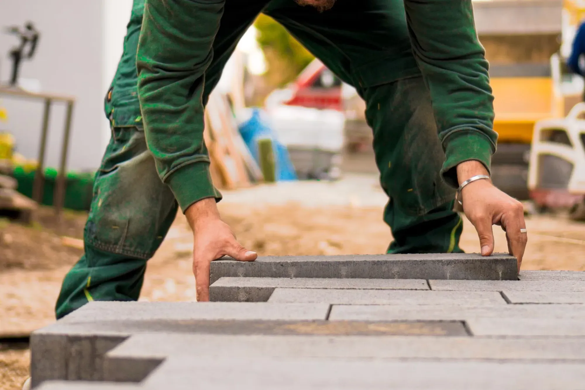 Hands setting concrete pavers on a prepared sand base