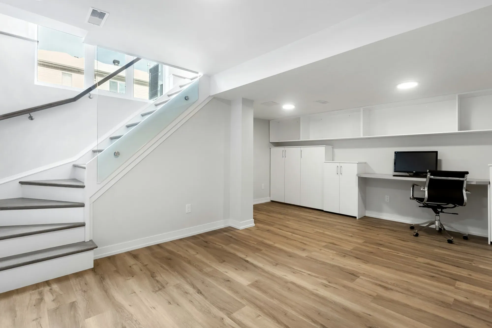 Finished basement with a staircase, window well, built-in desk and wood-look flooring