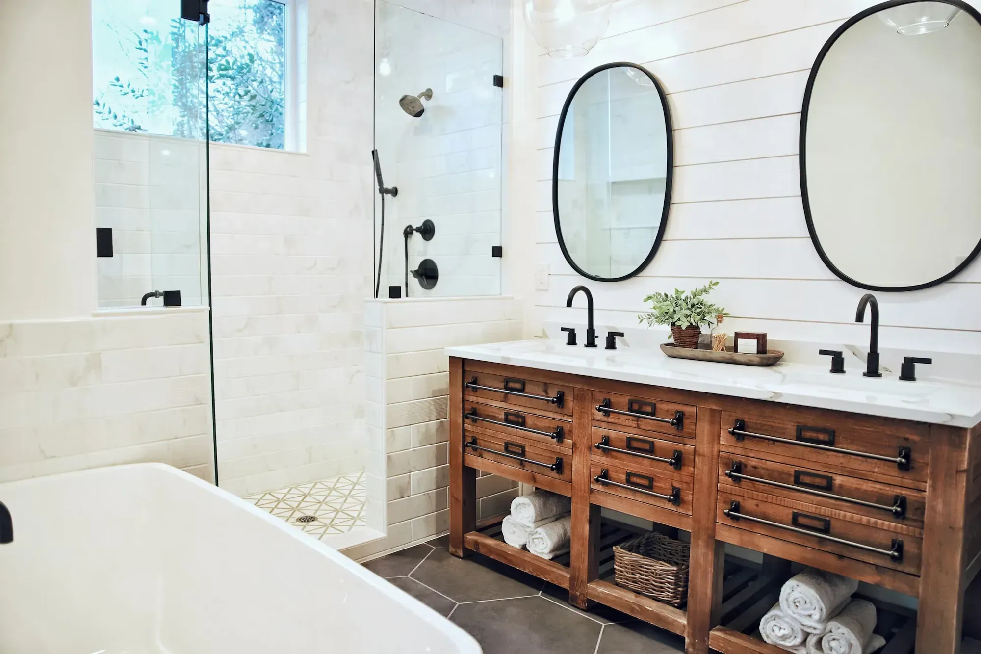 Remodeled bathroom with a freestanding tub, glass shower, wood vanity and twin mirrors