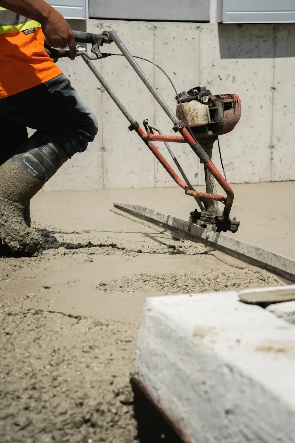 Worker finishing a freshly poured concrete slab with a power trowel