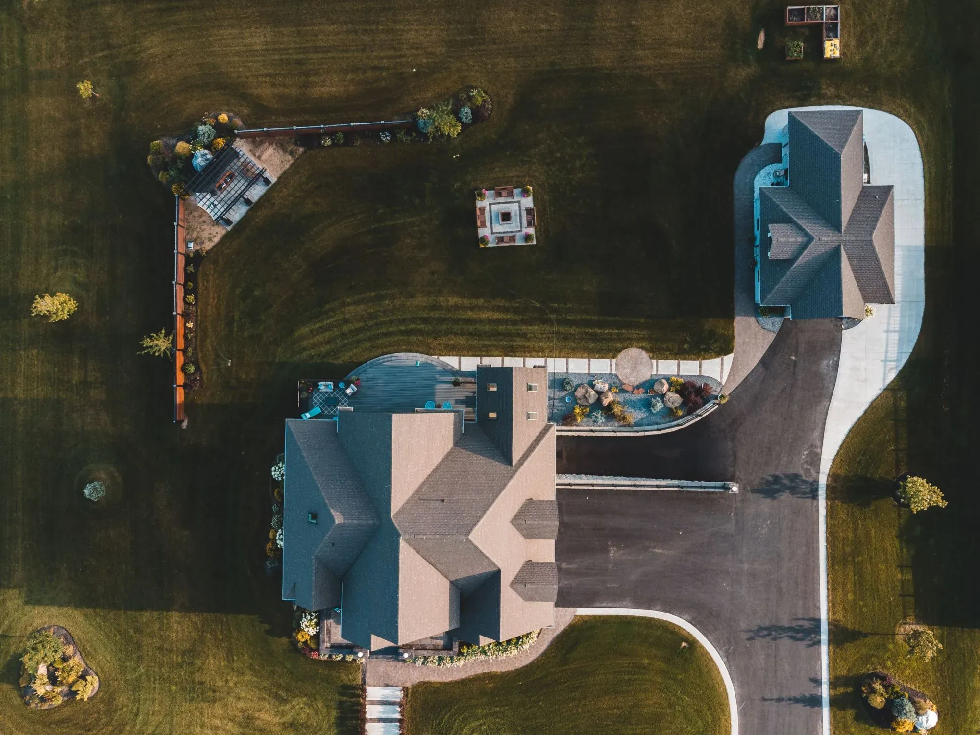 Aerial view of a wide lawn with landscaped beds, a fire-pit patio, a pergola and a long driveway