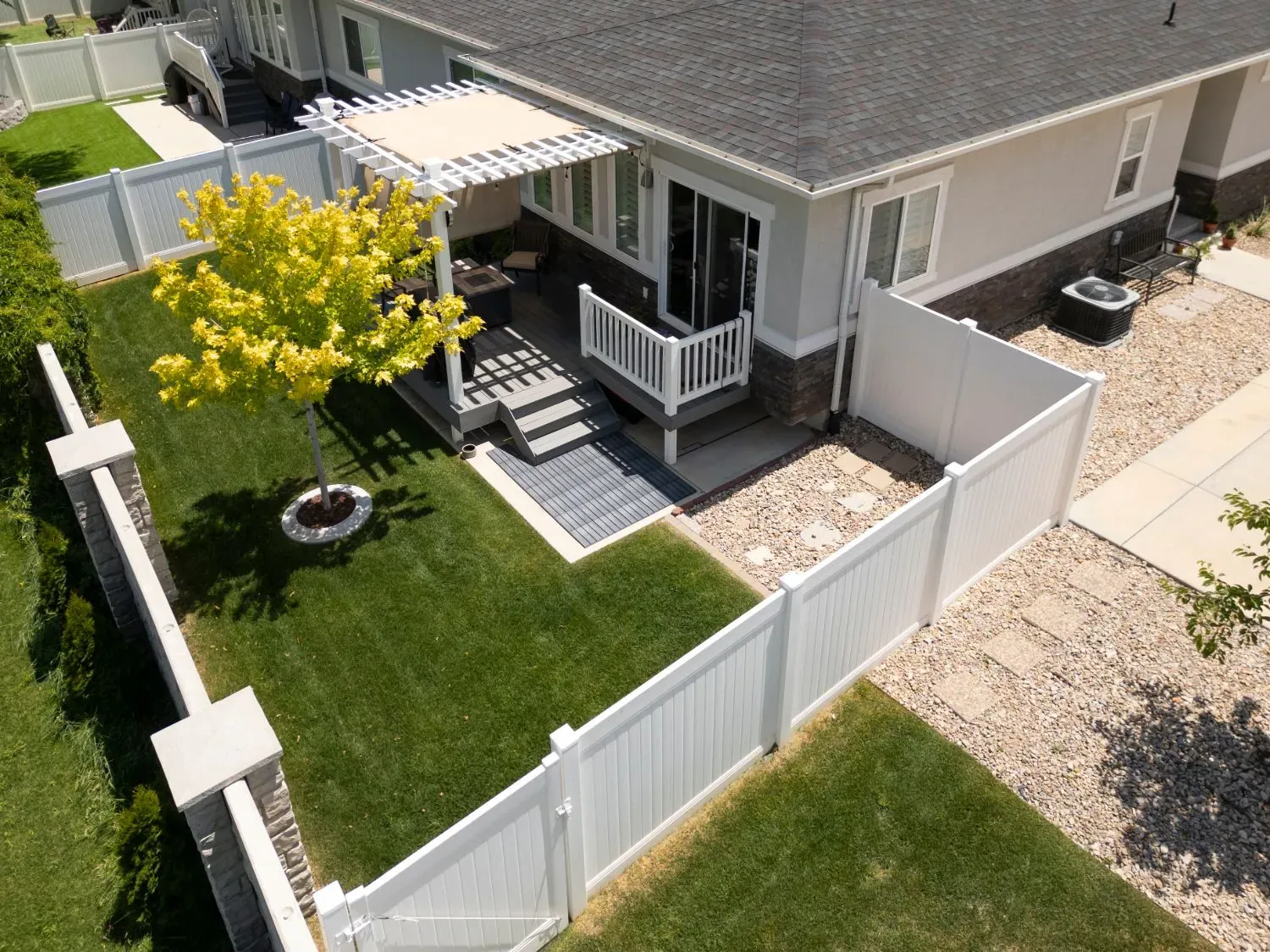 Aerial view of a white vinyl privacy fence and gate around a backyard lawn with a pergola-covered deck