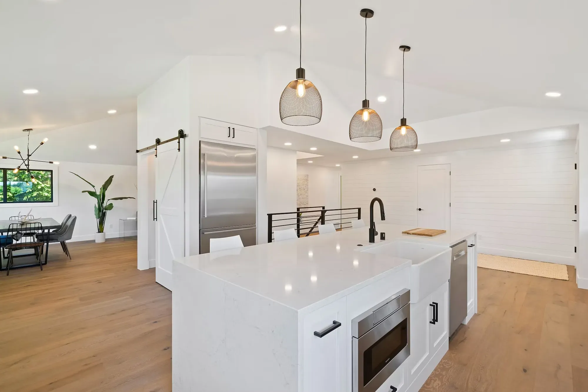 Open-plan kitchen and living area with a white island, pendant lights and wood floors