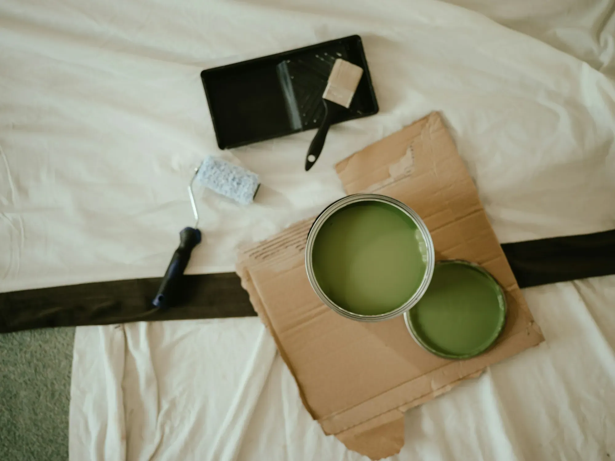 Open can of green paint, a roller, brush and tray laid out on a drop cloth