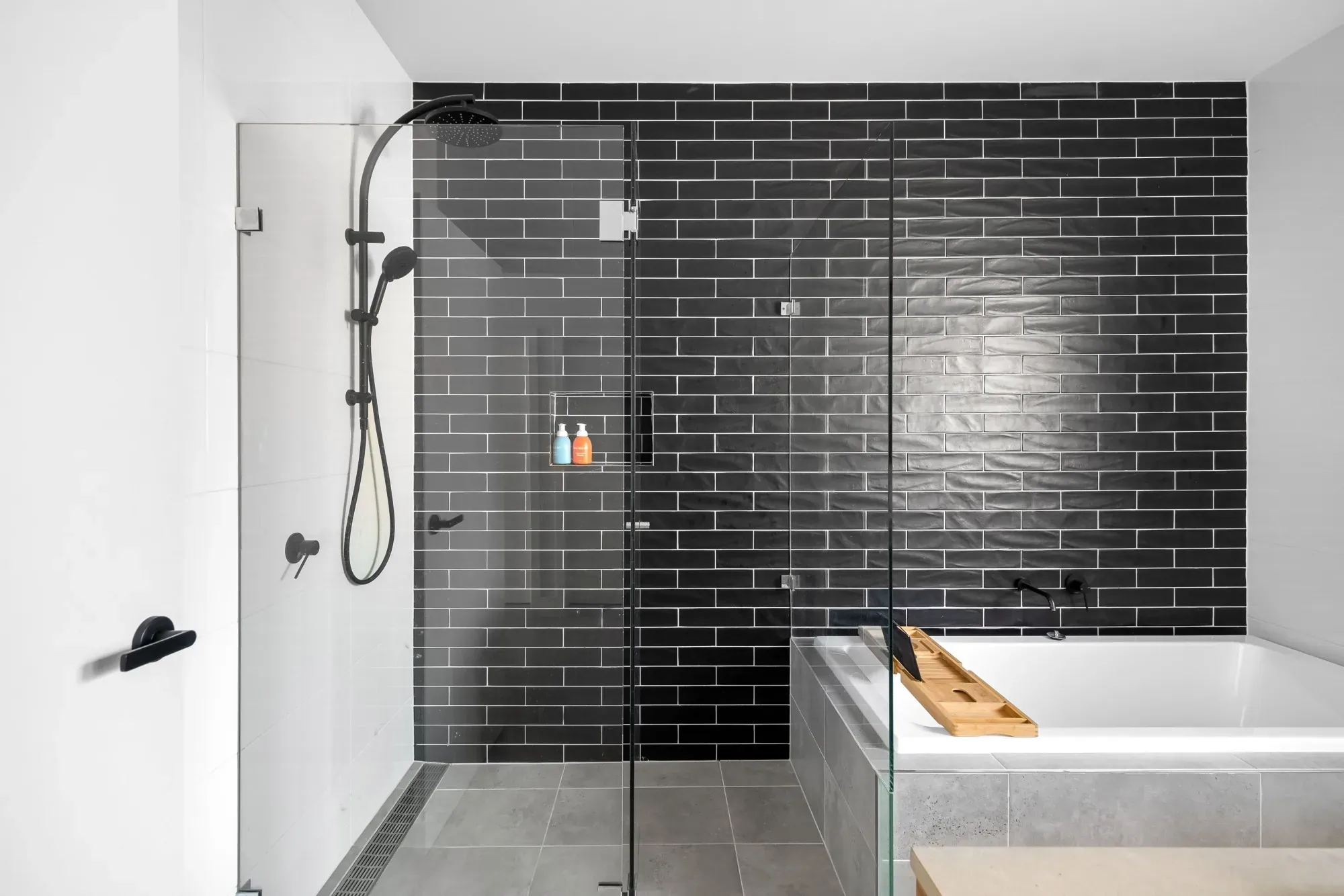 Bathroom with a glass shower, black subway tile and a built-in tub