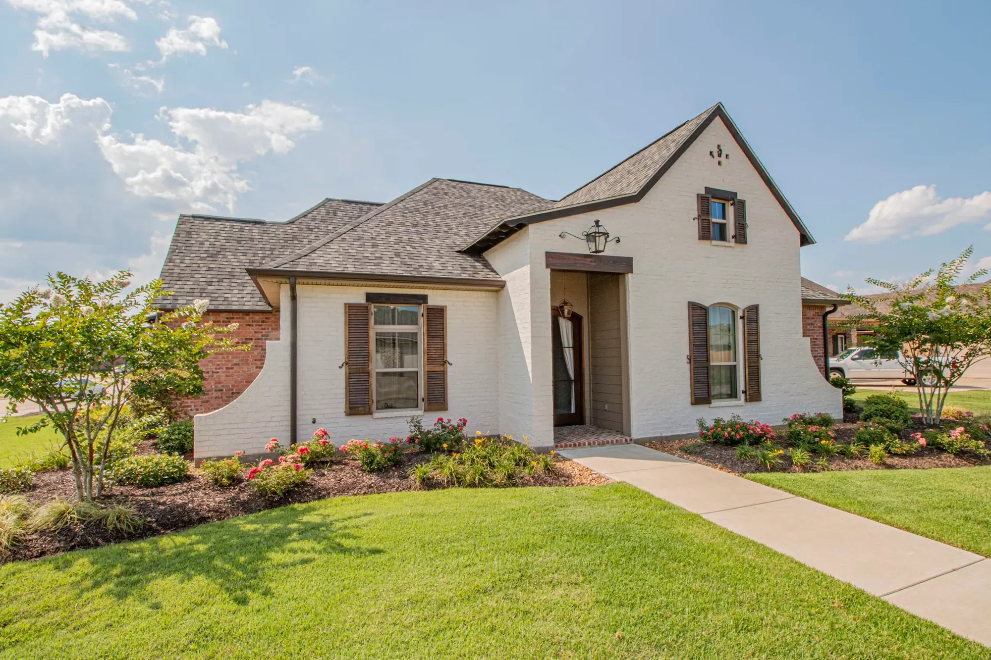 Fresh green lawn in front of a brick and stucco house with planting beds