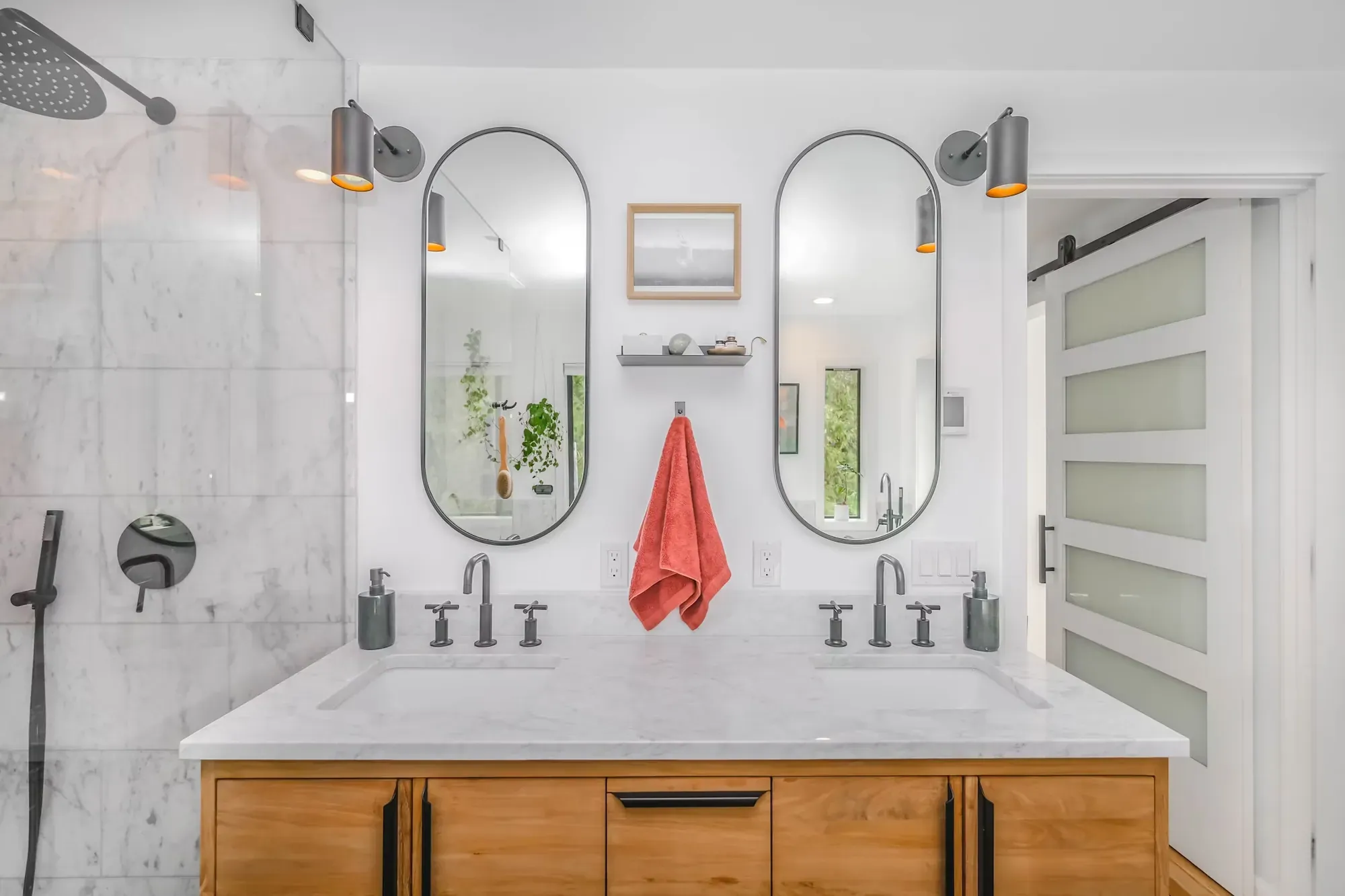 Marble-tiled shower wall beside a double vanity with arched mirrors